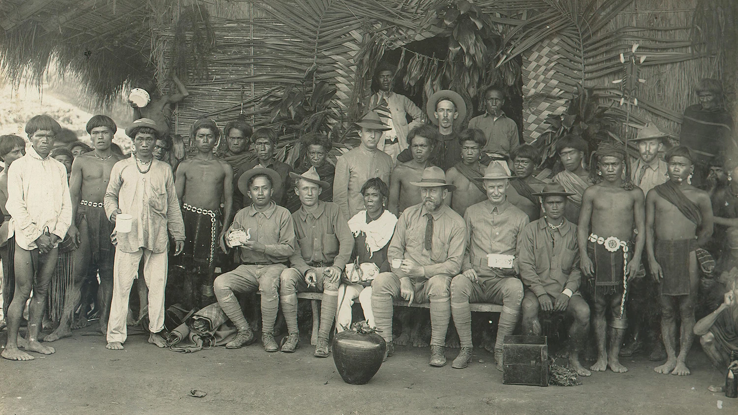 Two American colonial officials sitting with a group of Ifugao men in the Philppines.
